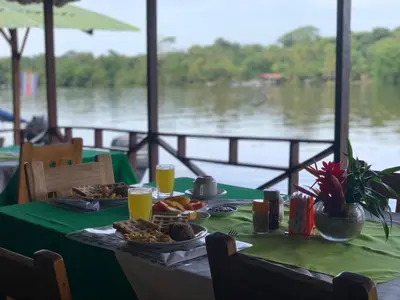 a green table with food and drinks on it with a view of a river at All Rankins Eco-Lodge in Tortuguero