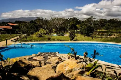 a large blue swimming pool with rocks in a yard at Colinas del Miravalles Hotel & Hot Springs in Hacienda Guayabo