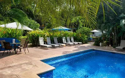 a swimming pool with chairs and a table and an umbrella at Tamarindo Blue Apartments in Tamarindo