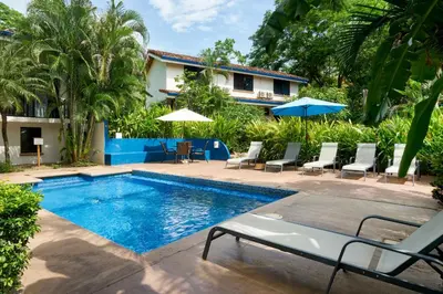 a pool with chairs and umbrellas next to a house at Tamarindo Blue Apartments in Tamarindo