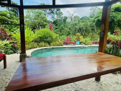 a wooden table sitting next to a swimming pool at Macaw Villa - Riverfront With A Pool in Uvita