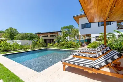 a swimming pool with two lounge chairs and a house at La Joya de Nosara in Playa Pelada