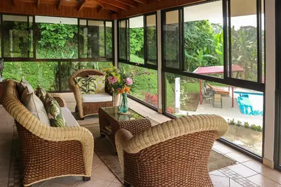 a screened in porch with wicker chairs and a table at Casa Garrobo in Dominical