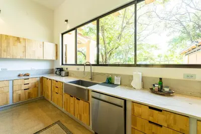 a kitchen with wooden cabinets and a large window at Casa Cenizaro- 4Br House In Hacienda Pinilla in Tamarindo