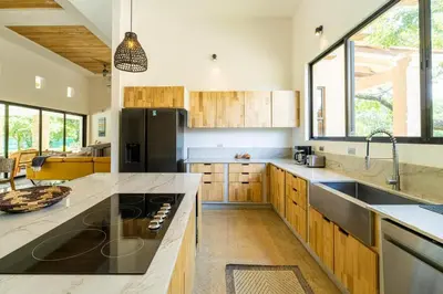 a kitchen with wooden cabinets and a black refrigerator at Casa Cenizaro- 4Br House In Hacienda Pinilla in Tamarindo