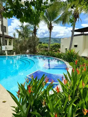 a large blue swimming pool with palm trees and flowers at Modern Condo with a Rooftop Patio in Liberia