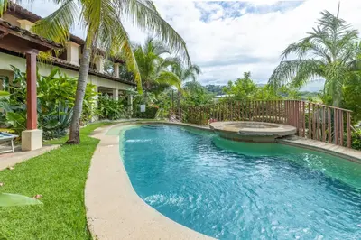 a swimming pool next to a house with palm trees at Stylish & Comfortable Condo with Balconies in Liberia
