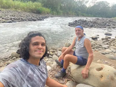 two people sitting on rocks next to a river at Finca Bambú Del Valle in Santa Clara