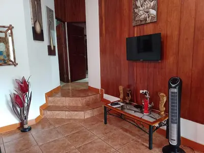 a living room with a table and a tv on a wall at Natural Pacific Suites, Manuel Antonio-Quepos-Hotel in Manuel Antonio