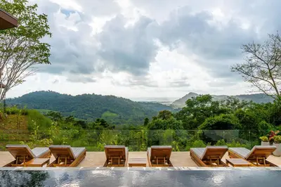 a group of chairs and a pool with mountains in the background at Casa Grande del Mar - by Pura Villas in Punta Mala