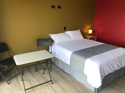 a bedroom with a bed and a table and a chair at Hotel Hospedaje Alto Lechuza Zarcero in Zarcero