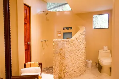 a bathroom with a stone shower with a toilet at Tamarindo Village Hotel in Tamarindo