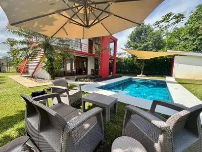 a patio with chairs and an umbrella and a pool at La Casa Pina Pacifica near La Fortuna in San Ramón