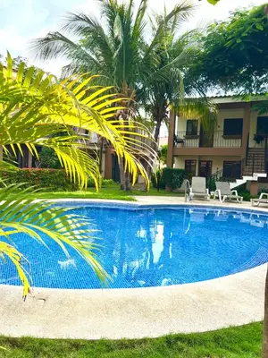 a large blue swimming pool with palm trees and a building at The Beach House Ground Floor Condo in Coco