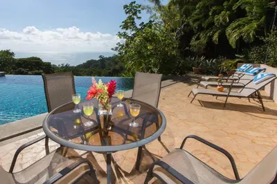 a glass table with wine glasses and flowers on a patio at Colores del Viento - by Pura Villas in Uvita