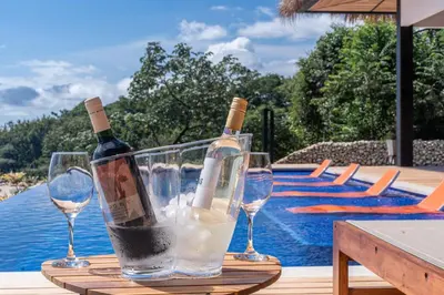two wine bottles and glasses on a table near a swimming pool at Villa Setai - Full Ocean view in Santa Teresa Beach