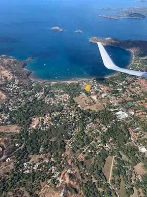 an airplane wing flying over a city and the ocean at Toro Blanco in Coco