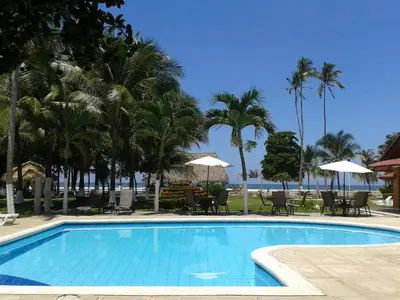 a swimming pool with chairs and umbrellas and palm trees at Hotel & Villas Tangerí in Jacó