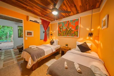 two beds in a room with orange walls at Jungles Edge Hotel, Jiu Jitsu, Muay Thai Retreat Center in Nosara