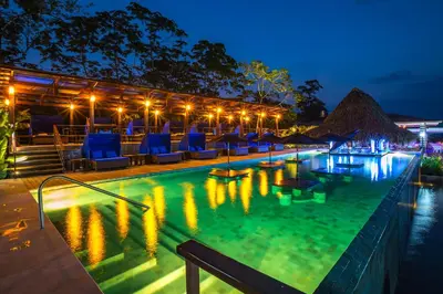 a swimming pool at night with chairs and umbrellas at Nayara Springs - Adults Only in Fortuna