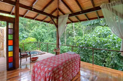 a room with a bed on a deck with a view of the forest at Nayara Springs - Adults Only in Fortuna
