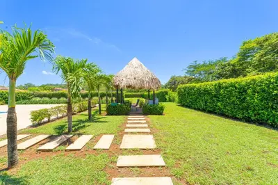 a garden with a grass umbrella and palm trees at Casa Callie- 3 Bedroom House With Pool in Tamarindo