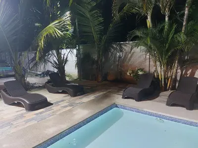 a swimming pool with chairs and palm trees at Casa Dñ Ana in Jacó