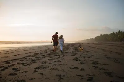 a man and woman walking on the beach with a dog at Encantada Ocean Cottages in Esterillos Este
