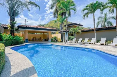a swimming pool in front of a house with palm trees at Condo Las Brisas near to Marina Herradura, free Pool and wifi in Herradura