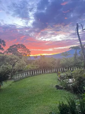 a sunset over a field of grass with a fence at Botanica Gardens and Eco Lodge in San Gerardo