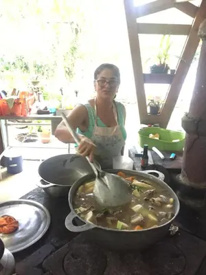 a woman stirring a pot of food with a spoon at Botanica Gardens and Eco Lodge in San Gerardo