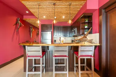 a kitchen with pink walls and a large island with stools at Luxury Condo with Panoramic Ocean Views, Sparkling Infinity Pool, and Modern Open-Concept Design in Playa Flamingo