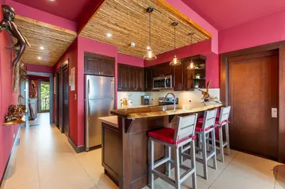 a kitchen with pink walls and a bar with stools at Luxury Condo with Panoramic Ocean Views, Sparkling Infinity Pool, and Modern Open-Concept Design in Playa Flamingo