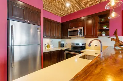 a kitchen with a stainless steel refrigerator and wooden cabinets at Luxury Condo with Panoramic Ocean Views, Sparkling Infinity Pool, and Modern Open-Concept Design in Playa Flamingo