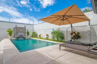 a swimming pool with an umbrella and a bench at La Casa de Papi. in Parrita