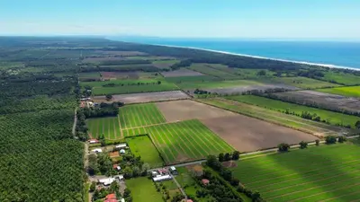 an aerial view of a farm with fields and the ocean at La Casa de Papi. in Parrita