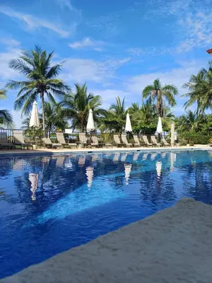 a large swimming pool with chairs and palm trees at Apartamento de Lujo en Playa Jacó, Frente al Mar, Wifi, AC, Parqueo Privado y Piscinas in Jacó