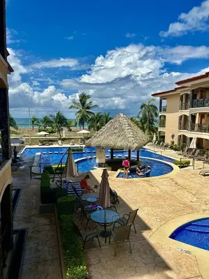 a pool with chairs and umbrellas next to a resort at Apartamento de Lujo en Playa Jacó, Frente al Mar, Wifi, AC, Parqueo Privado y Piscinas in Jacó
