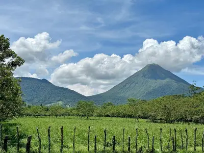 a mountain in the distance with a fence in a field at Oasis Arenal Villa Downtown Arenal Volcano View in Fortuna