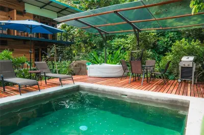 a deck with chairs and an umbrella and a swimming pool at Arenal Getaway in Fortuna