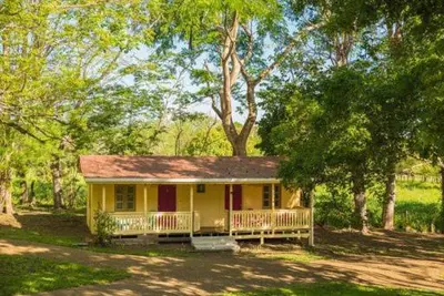 a small yellow house with a porch and trees at Villas La Paillote Costa Rica in Puntarenas