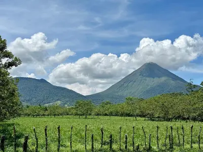 a mountain in the distance with a field and a fence at Oasis Arenal Villa Pool & Arenal Volcano View in Fortuna