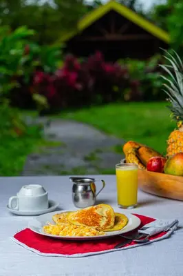 a table with a plate of eggs and a bowl of fruit at Selvita Lodge Arenal in Fortuna
