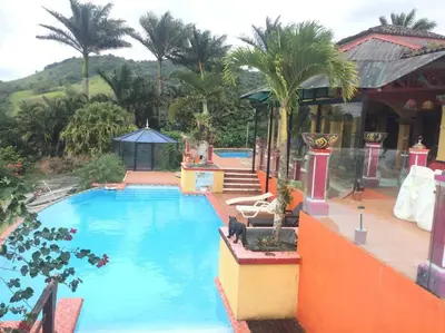 a large swimming pool with palm trees and a house at Lake Arenal Killer View Villa in Tilarán