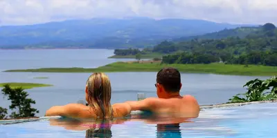 a man and a woman sitting in a swimming pool at Hotel La Mansion Inn Arenal in Nuevo Arenal