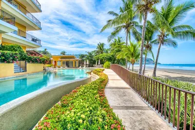a resort swimming pool with palm trees and a beach at SecretJaco - Luxury Beach Front Penthouse with Pool & Jacuzzi in Jacó
