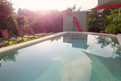 a swimming pool with chairs and the sun reflecting in the water at Boutique Tropical Retreat, Sleeps 10, Perfect for Friends and Fams in Sámara