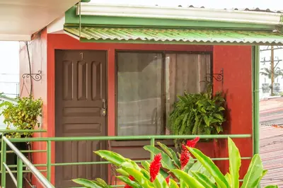 a red house with a door and a balcony at Hostal Nuevo Arenal downtown, private rooms with bathroom in Nuevo Arenal