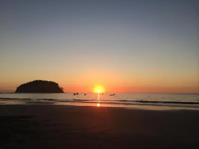 a sunset on the beach with people in the water at The Hideaway Hotel in Sámara