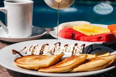 a plate of pancakes with whipped cream and fruit at The Hideaway Hotel in Sámara